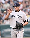 A man in a gray baseball uniform catches a baseball with his bare right hand. He is wearing a navy blue cap on his head with an interlocked "NY" and a black baseball glove on his left hand. His uniform reads "New York" across the chest.
