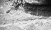 Photograph of archeological excavations at Fort Rock Cave, with tools and measuring instruments scattered about a rocky, dusty cliff area.