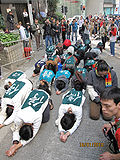 group of people prostrating in line each wearing a green top with the Chinese character for 'stop'