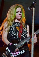 A woman with blonde hair and green streaks is playing the guitar.