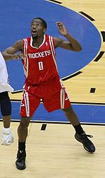 A basketball player, wearing a red jersey with the word "HOUSTON" and the number 0 on the front, stands on a basketball court.