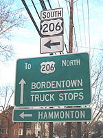 A shield for south U.S. Route 206 with a left arrow with two green signs below it. The top green sign reads to U.S. Route 206 north Bordentown truck stops with an up arrow and the bottom sign reading Hammonton with a left arrow.