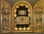 A golden, bejewelled triptych. The left and right wings each show three inlaid circular images; the centre panel has a scalloped surround housing two older triptychs, each containing a wooden Cross and showing Byzantine-style Greek lettering.