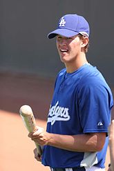 A man wearing a blue baseball jersey and baseball cap holding a light-colored wood baseball bat with both hands