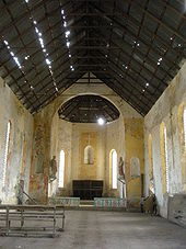 The altar of a church with a statue on either side, a white cross above, and light shining through the rafters