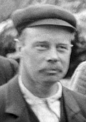 Fuzzy head-and-shoulders photo of a 40-year-old man in a cloth cap and mustache.