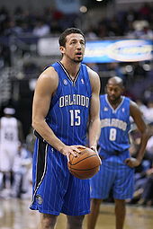 A basketball player, wearing a blue jersey inscribed with the word "ORLANDO" and the number 15 on the front, holds the ball at his waist as he prepares to shoot a free throw.