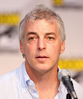 A headshot of a gray-haired man, opening his mouth to speak