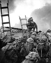 black & white photo of Marines using ladders to scale a seawall
