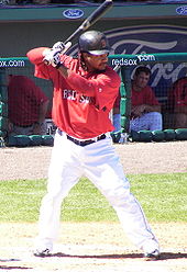 Batter in black hat red top and white pants, batting during spring training for the Red Sox.