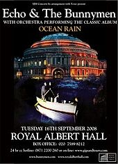 An poster advertising a concert with a black background and a picture of a circular building. Superimposed on the picture is a rowing boat with four men; two men are stood side-by-side at the back of the boat each holding an oar, the third man is sat in the centre of the boat and the fourth man is leaning over the front of the boat with his hand in the water. White text is on the poster at the top and the bottom giving details of the concert.