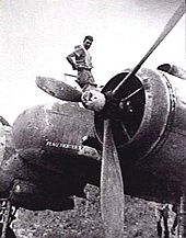 Man atop a twin-engined military aircraft, looking down at the camera