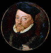 On a square black frame is a golden circle with a photo of a man with a brown beard and black garments with a white ruff on a starry background.