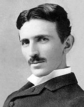 A black and white picture of a moustachioed dark haired man looking at the camera.