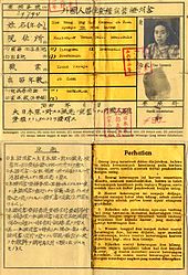 An old document made of one sheet of paper showing two outlined boxes, one in the top half and one on the bottom. The top box has writing in Japanese with a translation and a small head shot of a woman with a thumbprint below it. There are several small square imprints in red ink from a stamp. The bottom box is split into two vertical halves, one in Japanese and the other in Indonesian.