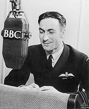 A man in dark, formal military uniform leaning forward towards a microphone labelled "BBC".