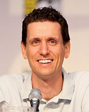 A man with brown hair, leans forward slightly to speak into a microphone.