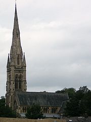 A stone church seen from a slight angle at the southwest, with a tower and tall spire on the left and the body of the church extending to the right