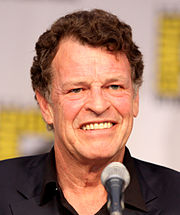 A dark-hair man in a black collared shirt staring straight at the camera, next to a microphone.