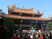 A temple decorated by dragons and other mythical animals. People are gathered in front of it and some of them are praying.
