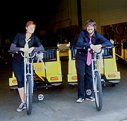 Young woman at left and young man at right, both wearing navy blue, standing on two yellow pedicabs.