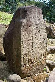 An upright stone slab with the front face flat and inscribed with two elaborately dressed figures facing each other, with a double column of hieroglyphs between them.