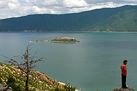 The island of Golem Grad in the dark blue water of Lake Prespa, surrounded by hills and mountains