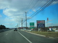 A four lane divided highway in a commercial area with a sign on the right side of the road reading Ridgedale Avenue Florham Park Parsippany upper right arrow all turns upper right arrow Morristown Airport right arrow