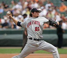 A man in a pinstriped gray baseball uniform throws a pitch with his right hand. His uniform reads "Minnesota" in red letters, and he wears a black baseball glove on his left hand.