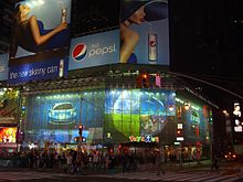 Outside of large, brightly lit store at night in New York City, surrounded by advertisements
