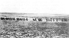 A line of men on horses charge across an open field towards the camera