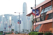 street shot showing blue and red advertising banners on street lamps with the words 'Act Now', Hong Kong's skyline in the background