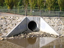 A large concrete hole opens out on a steep slope above muddy water