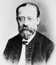  Portrait of balding, bearded, bespectacled middle-aged man with solemn expression, wearing a bow tie and high-buttoned jacket