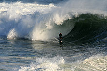 Photo of surfer at bottom of wave, attempting to let tube envelop him