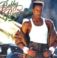 An African American man. He looks towards the camera with a commanding face. He wears a white wifebeater, jeans and a brown leather jacket. The background is a blurred street, with a truck behind him. On the upper left corner of the image, the words "Bobby Brown" are written in flourished red and green letters. On the upper left corner, the word "My Prerogative" is written in very small white capital letters.