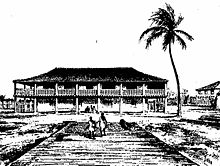 A large building in the background with the silhouette of a palm tree on the right and two people in the foreground