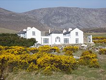 Charles Boycott's house on Achill Island. It is a large white house with two storeys; the mountainous terrain on the island is seen in the background.