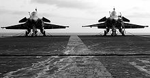 Landscape photograph of two jet parked side-by-side on carrier deck, with faint white line running down the middle.