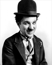 A smiling man with a small moustache wearing a bowler hat and a tight-fitting necktie and coat