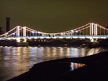 Night view of a lit suspension bridge over a wide river, which reflects the light from the bridge.