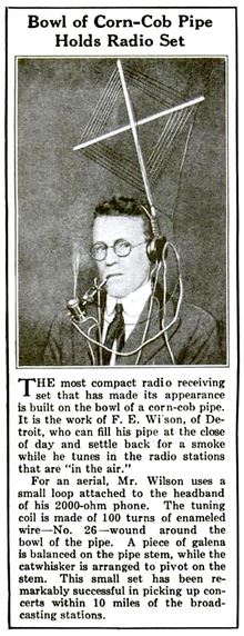  Newspaper clipping with photo showing a man wearing headphones and smoking a pipe; attached to the headphones is a diamond-shaped multiturn aerial, and the pipe bowl is wound with wire; the crystal detector is mounted on the pipe stem. Text in the clipping describes the photo and says this rig could pick up stations up to 10 miles away.