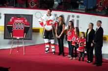 a man is pictured along side his wife and three daughters as he is presented with a framed hockey jersey with the numeber 1000 on its back.