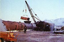 A crane shown loading contamined ice into a large steel tank.