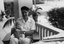 David Bushnell is seated on a porch and holding a baby.