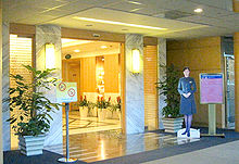 Lounge entrance. An open marble doorway flanked by two light sconces, potted plants, and three signs. Inside is a wood-lined hallway.