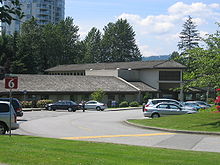 A small building surrounded by trees, with a parking lot in front of it.