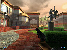 A screenshot of an early development version of the game. The image shows the male player character holding a gun, in a courtyard, next to a building.