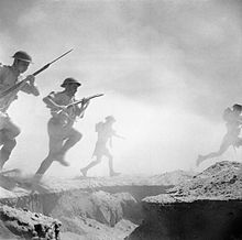 period photo of helmeted soldiers with rifles running through dust and smoke