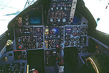 Cockpit of jet fighter with circular dials and gauges. A control stick protrude from between where the pilot's legs would be.
